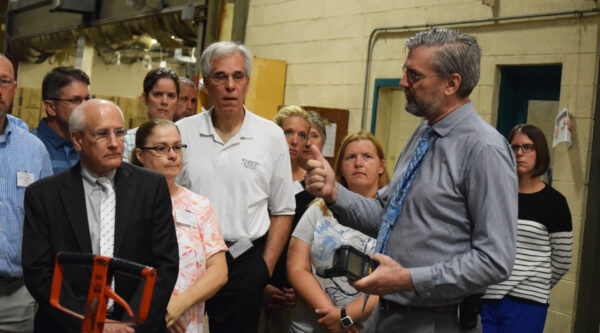A man in a suit leads a group of adults on a tour through a warehouse facility.