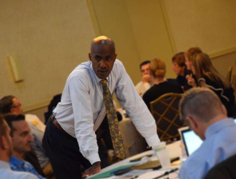 Dr. Tyrone C. Howard leaned over a desk in discussion with a group of educators at the 2019 BCIU Leadership Series