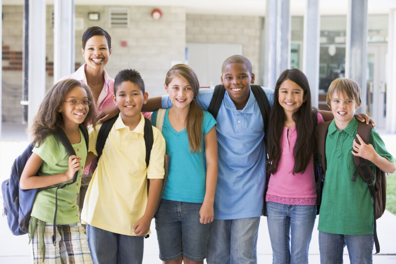 Diverse group of school children posing with teacher in hallway