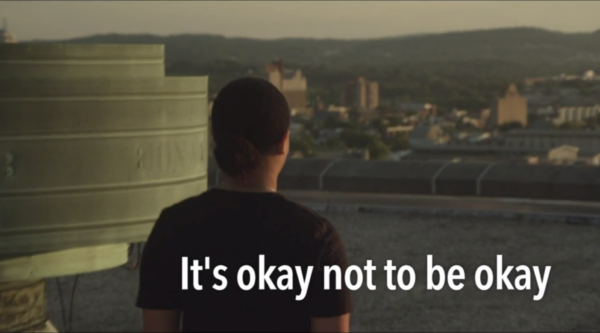 Screen capture from a PSA with a student looking out over a city and the caption "It's okay not to be okay"