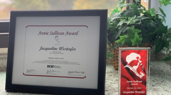 Photo of a framed certificate next to an engraved trophy that says "2020 Annie Sullivan Award Jacqueline Westerfer"